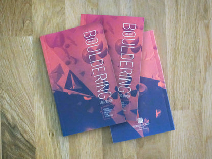 Three copies of "Bouldering Log Book" - one V0–V13 version, one V0-V18 version, and one showing the back cover with the Roaming Lines Studio mark. 